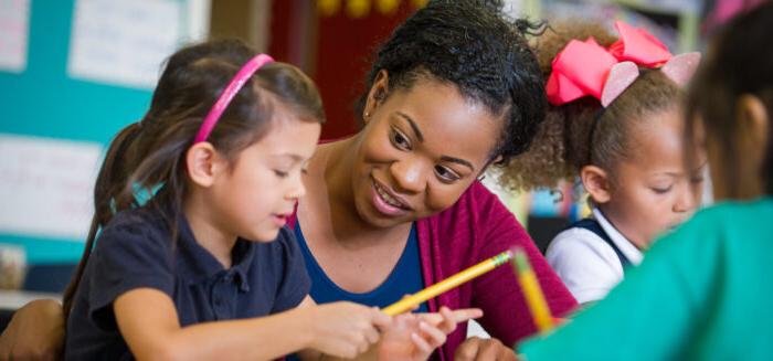 Female teacher with elementary age girl at school desk.